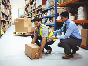 Supervisor shows worker how to lift heavy box in warehouse